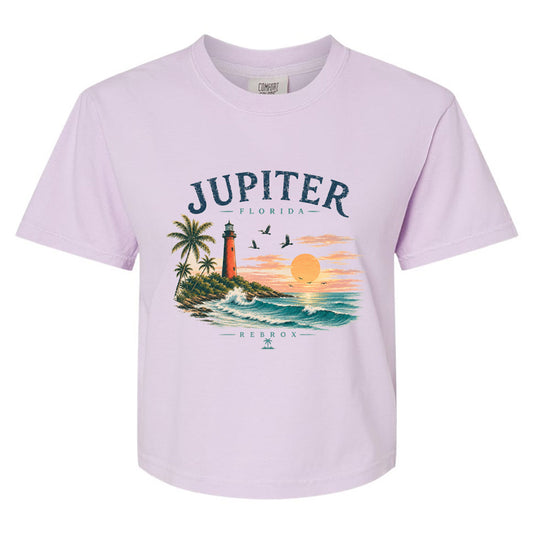 A light lavender short-sleeve crewneck t-shirt featuring a colorful graphic print of a tropical Florida sunset with a lighthouse, palm trees, and the text 'JUPITER - FLORIDA' and 'REBROX'.