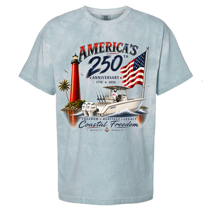 A light blue short-sleeve t-shirt with a detailed graphic print celebrating the 250th Anniversary of the United States. The graphic features a red lighthouse, a white sailboat, an American flag, and text reading 'AMERICA'S 250th ANNIVERSARY 1776 - 2026' and 'Coastal Freedom'.